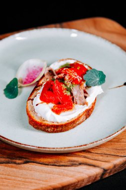 Tahta tabakta taze sebze ve krem peynirle kaplı lezzetli bir dilim ekmek.