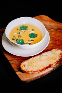 Taze yapraklar ve ahşap tabakta kızarmış ekmekle servis edilen kremalı çorba.
