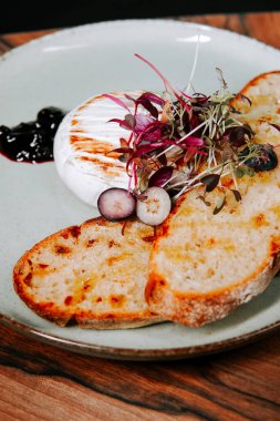 Köy tabaklarında kızarmış ekmek ve mikroyeşilliklerle servis edilen lezzetli taze burrata peyniri.