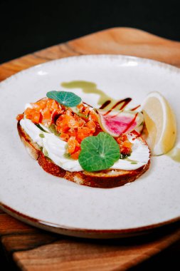 Somon, krem peynir ve ahşap bir tahtanın üzerinde taze sebzeli leziz açık yüzlü sandviç.