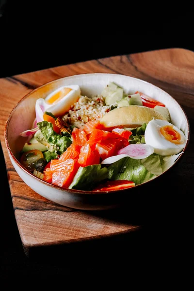 Renkli sebzelerle taze salata kasesi ve ahşap tahtada servis edilen haşlanmış yumurtalar.