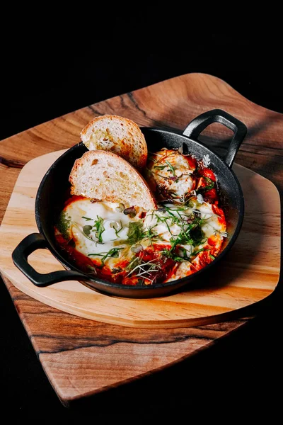 Domatesli nefis pişmiş yumurta ve ahşap tabakta kızarmış ekmekle servis edilen otlar.