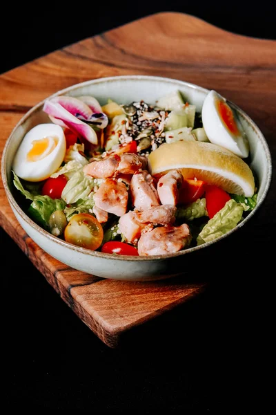 Tahta bir kasede servis edilen taze sebzeli ve yumurtalı sağlıklı tavuk salatası.