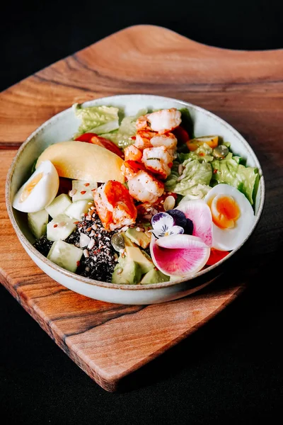 Tahtada karides, sebze ve yumurta bulunan renkli salata.