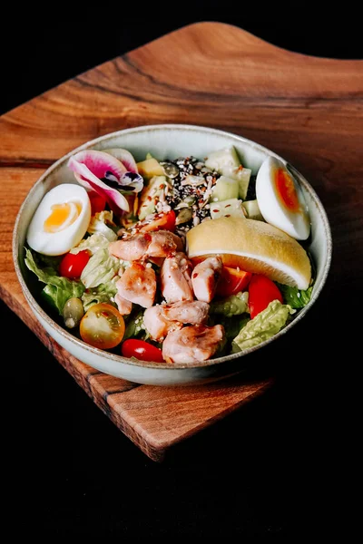 Taze salata kasesi ızgara tavuk ve ahşap tabakta servis edilen renkli malzemeler.