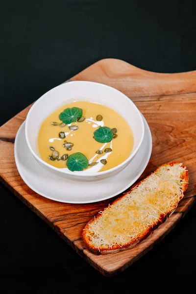 Kremalı çorba, ahşap kesme tahtasında yeşil garnitürlü kızarmış ekmekle servis edilir.