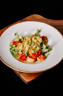 Çeri domatesli karides fettuccine ve ahşap bir tabakta taze otlar.