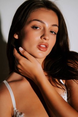 Kadın, atletik vücut ve güzellik sergileyen bir stüdyo ortamında iç çamaşırlarıyla rahatça poz veriyor.