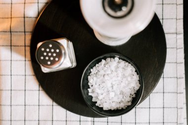 Koyu bir ahşap tepside, yanında titretici olan bir kasede düzgünce dizilmiş leziz tuz taneleri.