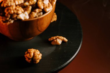 Ceviz dolu bir kasenin yanında, koyu ahşap bir masada soyulmuş ceviz.