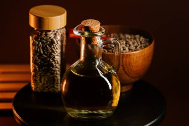 Tahta bir kâse ve karanlık bir yüzey üzerinde cam kavanozda tohumlarla sergilenen ayçiçeği yağı.