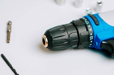Close view of a cordless drill on a white surface with tools scattered around