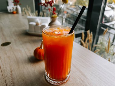 Tahta bir masada, küçük bir balkabağının yanında bardakta taze portakal suyu.