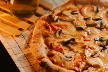 Peynirli, tavuklu ve mantarlı lezzetli pizza, ahşap bir masada, rahat bir ortamda.