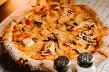 Mutfak ortamında servis edilen peynirli, tavuklu ve mantarlı taze pişmiş pizza.