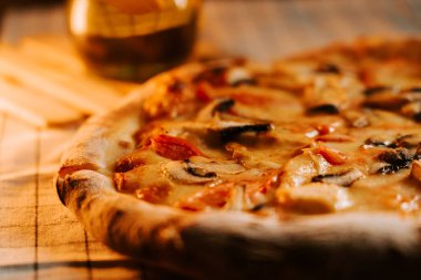 Peynirli, tavuklu ve mantarlı pizza ahşap bir masada sıcak ışıkla servis edilir.