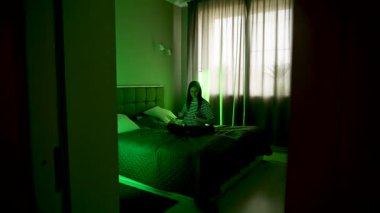 Kadın, odada doğal ışıkla otururken dizüstü bilgisayarda müzik dinliyor.