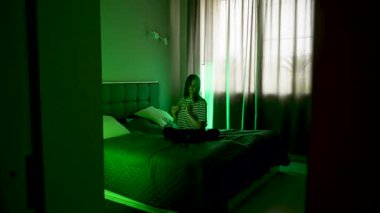 Kadın rahat bir odada yatarken dizüstü bilgisayarda müzik dinliyor.