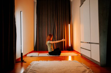 Genç bir kadın akşam saatlerinde evde yoga yapıyor.