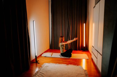 Genç bir kadın akşam saatlerinde hafif ışıkla yoga yapıyor.