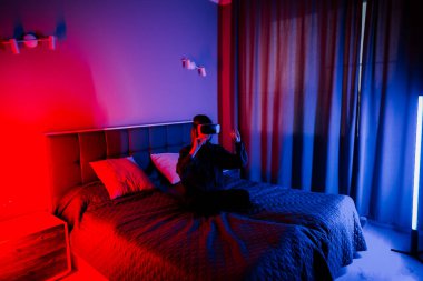 Genç kadın, gece boyunca loş ışıklı odada yatarken sanal dünyayı keşfediyor.