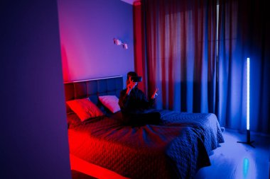 Sanal gerçeklikteki genç kadın geceleri renkli ışıklarla yatakta oturuyor.