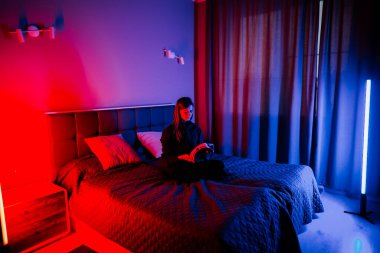 Genç bir kadın gece loş bir odada yatağında otururken sanal gerçeklik gözlüğü kullanıyor.