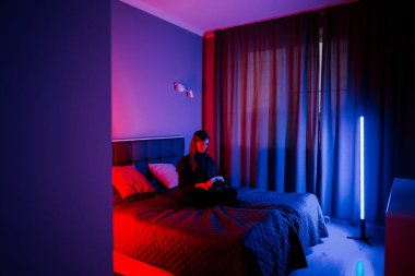 Genç bir kadın loş bir odada renkli ışıklarla sanal gerçekliği keşfediyor.