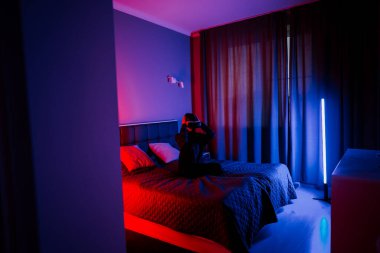Genç bir kadın gece vakti renkli ışıklandırmalı bir yatak odasında sanal gerçekliği deneyimliyor.