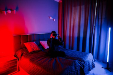 Genç bir kadın gece boyunca renkli ışıklandırmalı bir yatak odasında sanal gerçekliği keşfediyor.