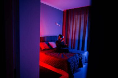 Genç bir kadın gece loş aydınlatılmış yatak odasında sanal gerçeklik gözlüğü takıyor.