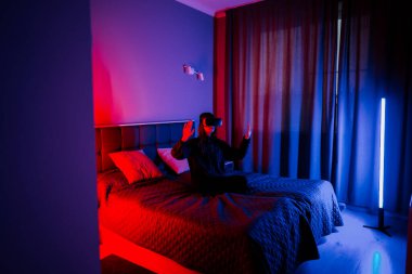 Genç bir kadın sanal dünyayı gece yatak odasında sanal gerçeklik gözlüğü kullanarak keşfediyor.