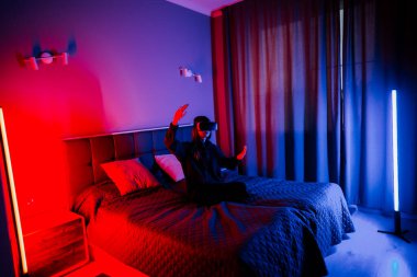 Genç bir kadın yatak odasında VR gözlükleriyle sanal dünyaları keşfediyor.