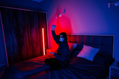 Genç bir kadın akşam saatlerinde yatak odasında sanal gerçeklik deneyiminden hoşlanır.