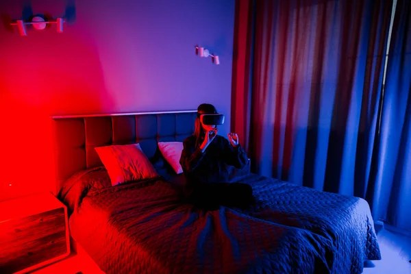 Genç bir kadın akşam saatlerinde yatak odasında sanal gerçekliği deneyimliyor.