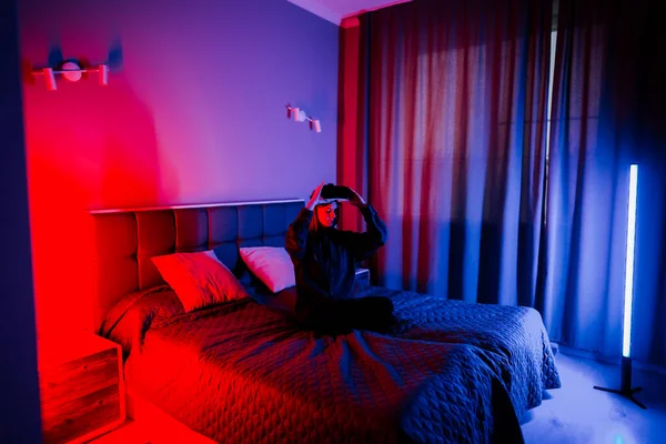 Genç bir kadın gece yatak odasında gözlük kullanarak sanal gerçekliği deneyimliyor.