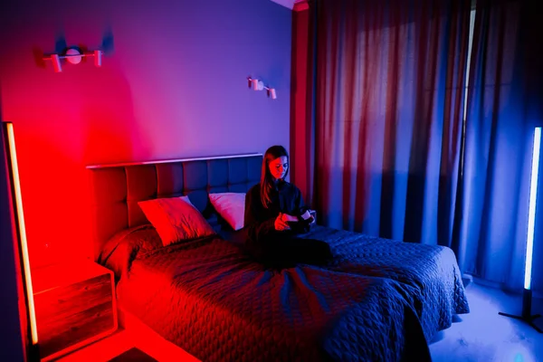 Genç bir kadın, gece vakti iyi aydınlatılmış bir yatak odasında sanal gerçeklik deneyiminden zevk alır.