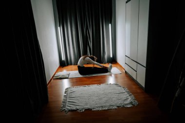 Genç kadın, esneklik üzerine yoğunlaşan bir çalışma sırasında evinde egzersiz yapıyor.