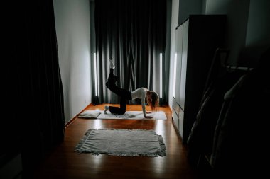 Genç bir kadın, akşam saatlerinde evdeki aydınlık alanda tek başına egzersiz yapıyor.