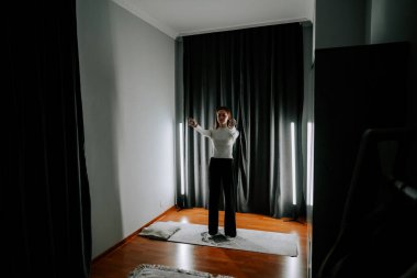 Genç kadın sabah antrenmanı sırasında perdenin önünde egzersiz yapıyor.