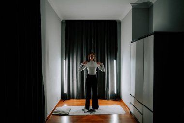 Genç kadın akşam saatlerinde evde aynanın önünde egzersiz yapıyor.