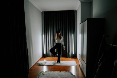 Genç bir kadın akşam saatlerinde sessiz bir odada egzersiz yapıyor.