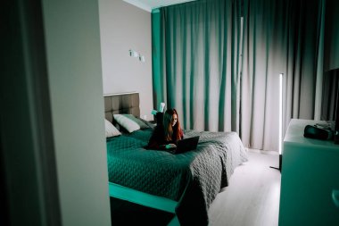 Genç kadın geceleri rahat bir yatak odasında yatarken dizüstü bilgisayarda ders çalışıyor.