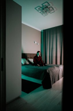 Genç bir kadın, yumuşak ışıklı bir yatak odasında yatarken dizüstü bilgisayarda ders çalışıyor.