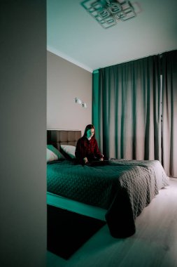 Genç bir kadın akşam vakti odasında yatarken dizüstü bilgisayarda ders çalışır.