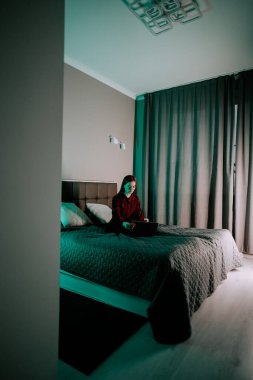 Genç kadın geceleri rahat bir odada yatarken dizüstü bilgisayarda ders çalışıyor.