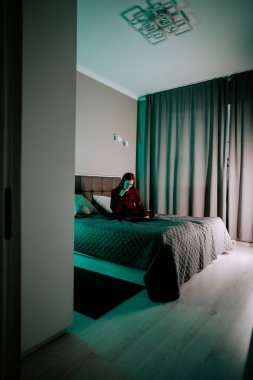 Genç bir kadın akşamları modern bir yatak odasında yatarken dizüstü bilgisayarda ders çalışıyor.