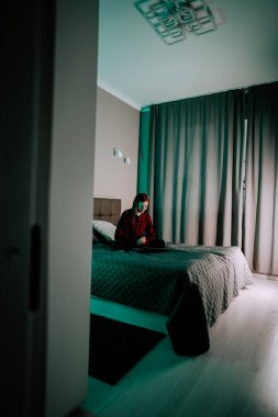 Genç kadın, akşam saatlerinde yatak odasında otururken dizüstü bilgisayarda ders çalışıyor.