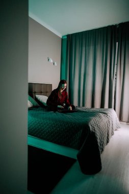 Genç bir kadın evdeki loş ışıklı bir odada yatarken dizüstü bilgisayarda ders çalışıyor.