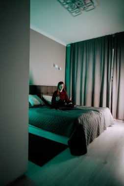 Gündüz vakti modern yatak odasında yatağında oturan genç bir kadın dizüstü bilgisayarda ders çalışıyor.